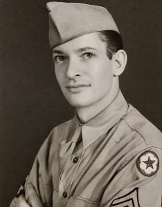 Portrait of a soldier in uniform and an overseas cap with a star patch on his sleeve.