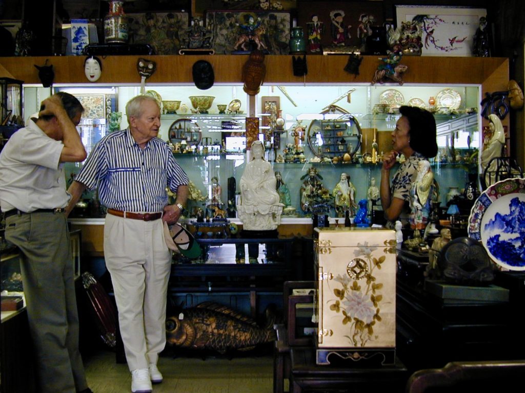 Two men and a woman in a shop filled with antique Asian art, figurines, and decor.